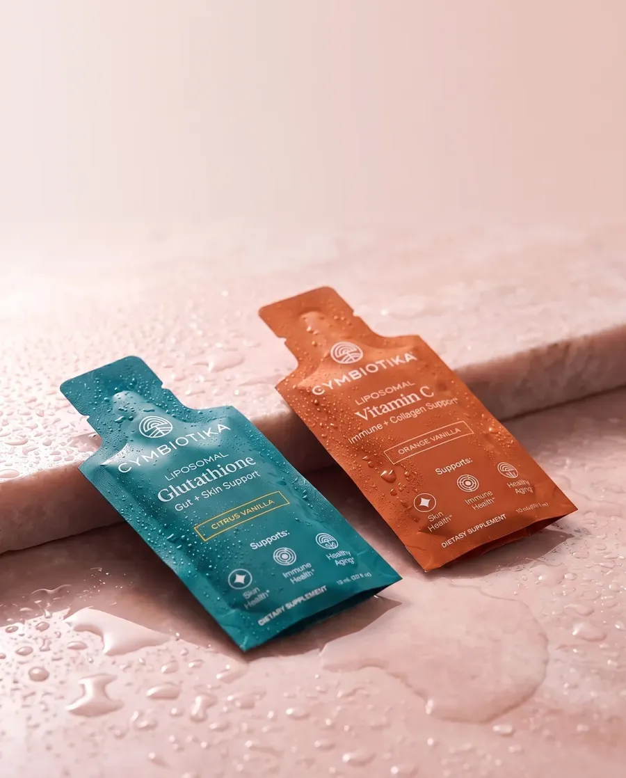 A Cymbiotika static ad: Glutathione and Vitamin C pouches on wet blush stone